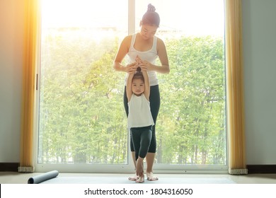 Asian mom practice yoga with a adorable daughter at home, try to teach young daughter to do yoga tree pose or vrksasana while exercise at home.
