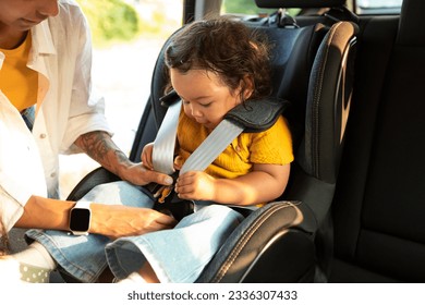 Asian Mom Sitting Down Her Toddler Daughter In Baby Car Seat, Adjusting Harness Straps For Safety During Automobile Journey. Cropped Shot, Closeup Of Child In Chair For Safe Auto Trip - Shutterstock ID 2336307433