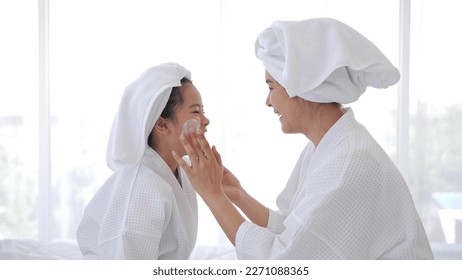 Asian mother adding treatment cream on the cheek to little girl with spa dress and head covered with a white towel on bed together at home - Powered by Shutterstock