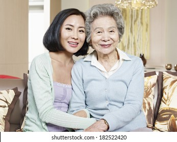 Asian Mother And Adult Daughter Sitting On Couch Smiling