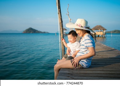 Asian mother and baby sit togather on the wooded bridge in resort on Koh Mak, Koh Mak and Kood is island in Thailand, This immage can use for family, summer, holiday, love, and beach concept
