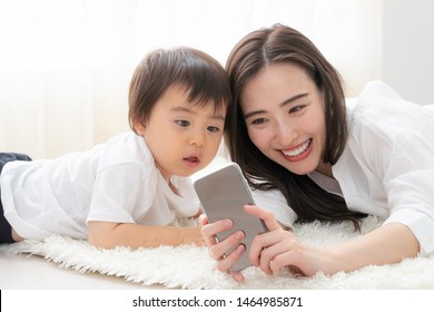 Asian Mother And Baby Using Smart Phone In Living Room