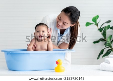 Asian mother Bathing her 7 month old daughter, which the baby smiling and happy, with white background,  to Asian family and baby shower concept.