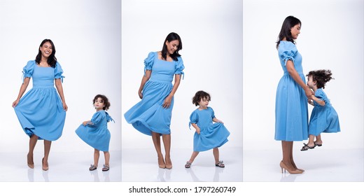 Asian Mother And Caucasian Daughter Stand And Wear Same Blue Blouse Dress Together. Little Girl Hold Mom Hand And Smile With Love. White Background Isolated