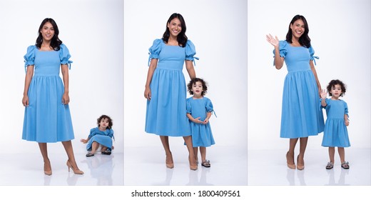 Asian Mother And Caucasian Daughter Stand And Wear Same Blue Blouse Dress Together. Little Girl Hold Mom Hand And Smile With Love. White Background Isolated