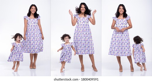 Asian Mother And Caucasian Daughter Stand And Wear Same Purple Flower Blouse Dress Together. Little Girl Hold Mom Hand And Smile With Love. White Background Isolated