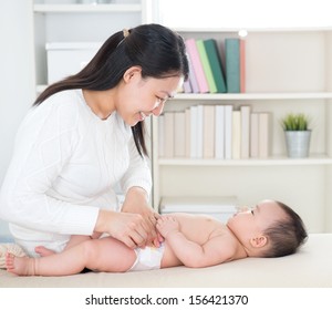 Asian Mother Changing Diaper To Baby Girl At Home.