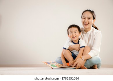 Asian Mother And Child Reading Book Together Concept. Vietnamese Mum And Son Sitting On Floor, Laughing While Flipping Pages Of A Story Book, White Background