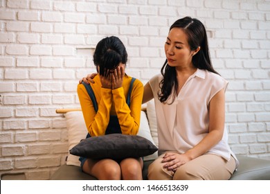 Asian Mother Comforting Crying Teenage Daughter In Miserable, Stressed, Depressed, Sad State Of Mind. 40s Mom Is Putting Hands Over This Adolescent Teenager Shoulders At Indoors Room.