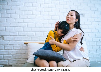 Asian Mother Comforting Crying Teenage Daughter In Miserable, Stressed, Depressed, Sad State Of Mind. 40s Mom Is Hugging This Adolescent Teenager Shoulders At Indoors Room.