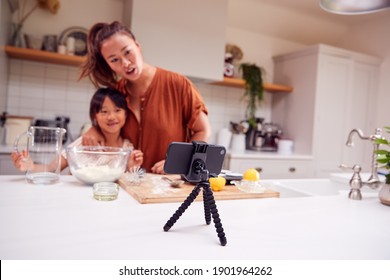 Asian Mother And Daughter Baking Cupcakes In Kitchen At Home Whilst On Vlogging On Mobile Phone