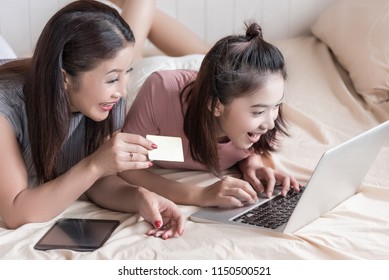 Asian  mother and daughter are lying with smiling face in the bedroom for shopping together on line via a laptop computer,using a credit card for shopping , happiness family and technology concept. - Powered by Shutterstock