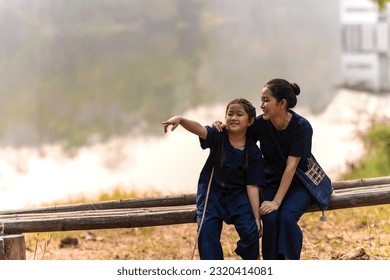 Asian mother and daughter in Northern indigo traditonal clothes sitting on woodbench and lake background having a good time together, mother and daughter relationship concept