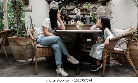 Asian Mother And Daughter Peevish Sitting On A Chair And  Faces Grumpy Expression