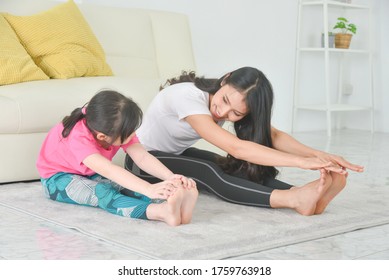 Asian Mother And Daughter Practicing Yoga Together At Home.Mother And Child Sitting And Stretching Their Body On The Floor.