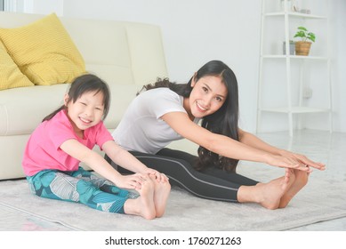 Asian mother and daughter practicing yoga together at home.Mother and child sitting and stretching their body on the floor.