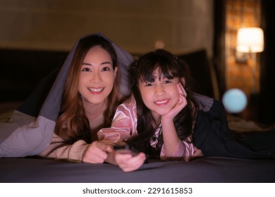 Asian Mother and daughter relax with tent and light in they bed room and read a teblet togather on night time at home