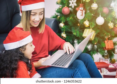 Asian Mother And Daughter Using Laptop Video Call Facetime Chatting Communication To Father With Decorating Christmas Tree In White Room At Home.Smiling Face And Happy To Celebrate New Year Festivel.