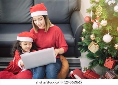 Asian Mother And Daughter Using Laptop Video Call Facetime Chatting Communication To Father With Decorating Christmas Tree In White Room At Home.Smiling Face And Happy To Celebrate New Year Festivel.