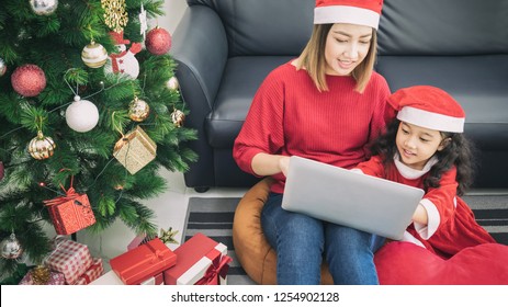 Asian Mother And Daughter Using Laptop Video Call Facetime Chatting Communication To Father With Decorating Christmas Tree In White Room At Home.Smiling Face And Happy To Celebrate New Year Festivel.