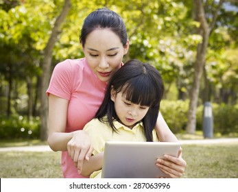 Asian Mother And Daughter Using Tablet Computer Outdoors.