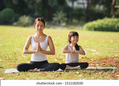 Asian Mother and daughter in white shirt and black trousers doing yoga exercises on grass in the park at the day time.sport and exercises for healthy lifestyle. - Powered by Shutterstock