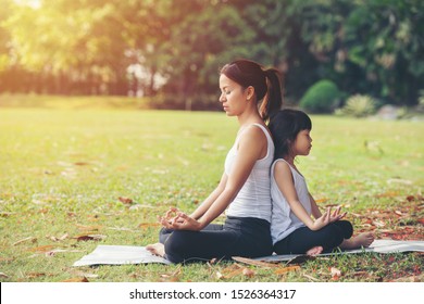 Asian Mother and daughter in white shirt and black trousers doing yoga exercises on grass in the park at the day time.sport and exercises for healthy lifestyle. - Powered by Shutterstock