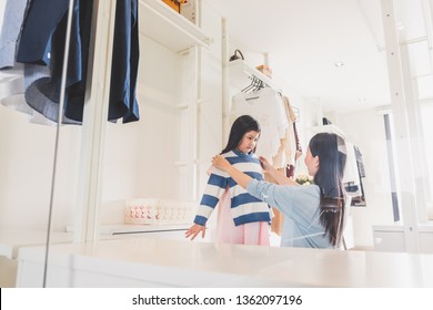 Asian mother dressing/choosing clothes to her girl daughter from wardrobe in bedroom, Asian family lifestyle concept - Powered by Shutterstock