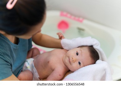 Asian Mother Dry Her Newborn Baby Hair With Towel After Rinsing Shampoo From The Hair In Bathroom. Mother Holding The Child With Care And The Child Is Smiling With Happiness.