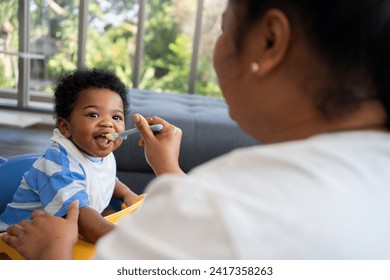 Asian mother feeding her 9 months old her cute little baby and African American helping for holding food plate At Home. Photo series of family, kids and happy people concept. Parents feed kids. - Powered by Shutterstock