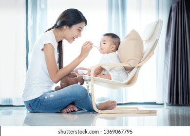 Asian Mother Feeding To Her Baby In Leving Room