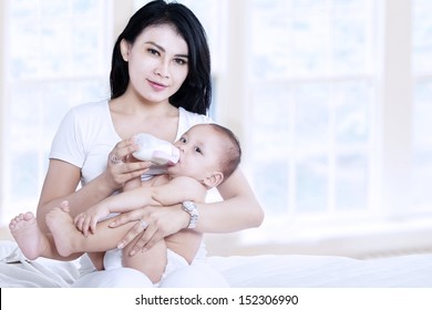 Asian Mother Feeding Her Baby With Milk At Home