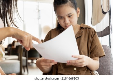 Asian mother hand pointing at poor grading from examination result report of her daughter