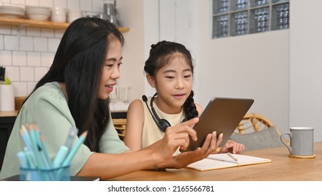 Asian Mother Helping Her Daughter Doing Homework, Learning Online At Virtual Class On Laptop Computer At Kitchen Table