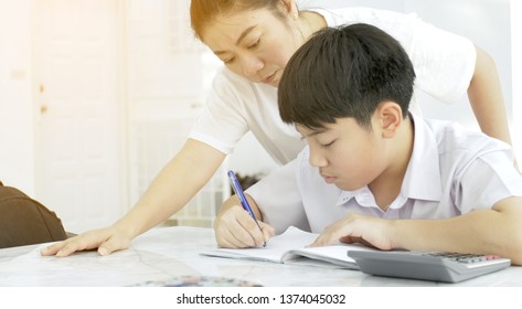 Asian Mother Helping Her Son Doing Homework On White Table.