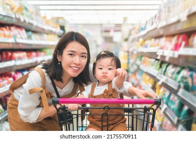 Asian Mother And Her Daughter Buying Food At Huge Supermarket , Baby Sit In Trolley, Family Shopping Concept.