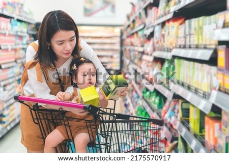 Asian mother and her daughter buying food at huge supermarket , Baby sit in trolley, Family shopping concept.