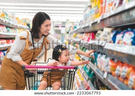 Asian mother and her daughter buying food at huge supermarket , Baby sit in trolley, Family shopping concept.