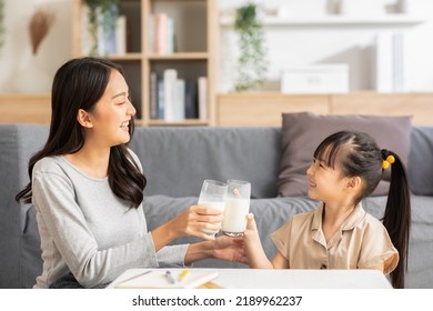 Asian Mother And Her Daughter Clink Glasses Enjoy And Smile With Milk Drink.Mom And Little Girl Holding Milk Glasses And Drink To Get Calcium.Healthy Eating Concept