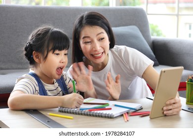 Asian mother and her daughter drawing together in online art class while waving to the teacher using digital tablet at home for homeschooling and video call concept - Powered by Shutterstock