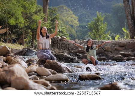 Asian mother and her daughter playing splash water on the river together with fun. Outdoor activity for family on vacation.