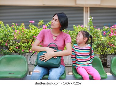 Asian Mother And Her Daughter Sitting At Bus Station. Mom And Child Girl Passenger Waiting For Public Transport.