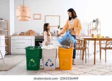 Asian mother with her little daughter sorting garbage with recycle bins in kitchen - Powered by Shutterstock