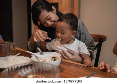 Asian Mother With Her Son Eating Together While Dinner. Mom Feeding Her Toddler Son