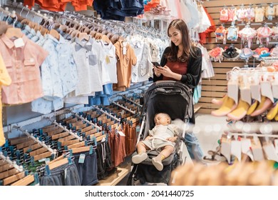 Asian Mother With Her Son Shopping In The Mall While Calling On Phone