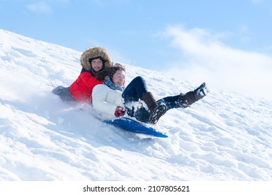 Asian mother and her son  sliding on sleds down snow hill in winter