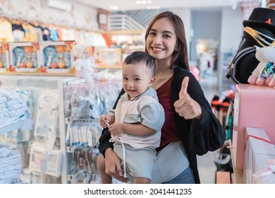 Asian Mother With Her Toddler Boy Shopping In The Baby Shop With Thumb Up