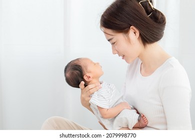 Asian mother holding baby in her arm, eye contact with newborn. Touching of love between motherhood task concept, mother lifting, looking toddler while son sleeping, new mom take care infant at home - Powered by Shutterstock