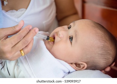 Asian Mother Holding And Feeding Medicine Syrup To Her Child  By Plastic Syringe