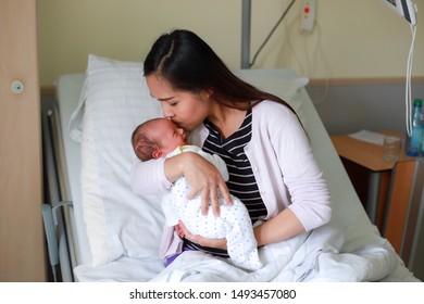 Asian Mother Holding Newborn Baby In Her Arms And Kissing In Delivery Room At Hospital After Giving A Birth.